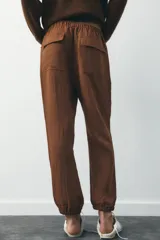 Pantalón jogger color gris claro, de tiro alto con cintura elástica ajustable con cordones, bolsillos delanteros y traseros con solapa, y puños elásticos en el bajo.