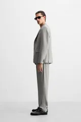 Pantalón de vestir gris claro con textura, corte regular fit, bolsillos laterales y traseros de doble vivo con botón. Cierre frontal con cremallera y botón.