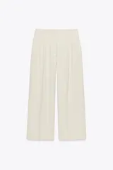 Pantalón color crema de tiro alto con trabillas, bolsillos laterales y pinzas. Cierre frontal con cremallera, botón interior y gancho metálico.