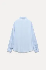 Camisa marrón de corte holgado, con cuello de solapa, manga larga con pliegues y bajo asimétrico. Cierre frontal con botones.