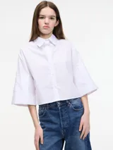 Camisa blanca cropped con botones en la parte delantera y mangas 3/4 con botones. Tiene pinza en la espalda.