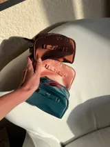 Neceser gris de tela satinada con cierre superior y detalle de moño en el frente.