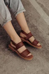 Sandalias de cuero marrón con tiras tejidas a mano y costuras a la vista, con base plana.