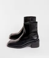 Bota corta de cuero charol negro, con caña baja, cierre lateral y taco cuadrado de madera.