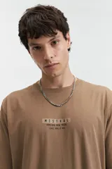 Remera color tostado de manga corta con cuello redondo y estampado frontal con texto "Mistral Kamioka New Trial Since 1976 // NLD".