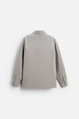Camisa color crema de corte relaxed fit, confeccionada en tejido de mezcla de algodón suave al tacto. Tiene cuello solapa, manga larga con puños abotonados, un bolsillo de parche en el pecho y cierre frontal con botones.