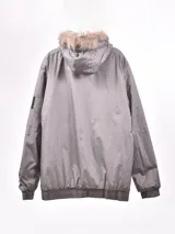 Campera gris con capucha con borde de piel sintética, cierre frontal con cremallera, bolsillos laterales con solapa y bolsillo con cremallera en la manga.