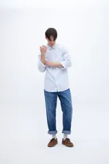 Camisa celeste con rayas verticales blancas, de corte regular, con cuello solapa clásico, bolsillo en el pecho y botones personalizados.