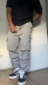Pantalón cargo color gris claro, de corte amplio, con múltiples bolsillos con solapa y ajuste con cordón en la cintura.