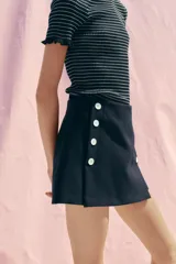 Falda pantalón corta color azul marino, de tiro alto y corte recto. Presenta doble hilera de botones blancos en el frente y cierre lateral con cremallera oculta.
