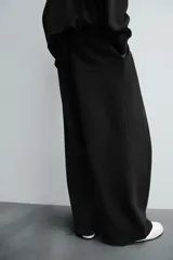 Pantalón jogger negro de corte relaxed fit, confeccionado en tejido de algodón. Presenta cintura elástica ajustable con cordón, pliegues frontales, bolsillos delanteros y un bolsillo trasero.
