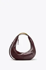 Bolso ovalado color borgoña de cuero sintético, con asa de hombro metálica dorada y cierre de cremallera.