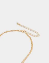 Collar corto multicadena dorada, con una cadena de eslabones y otra de perlas. Incluye dijes de zapatos de ballet rosados, moño y flor de metal dorados.