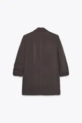 Blazer color marrón oscuro, abierta, con cuello solapa y hombreras. Manga tres cuartos con trabilla y botón dorado. Bolsillos delanteros con solapa.