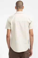 Camisa de manga corta color crema, confeccionada en algodón ligero con textura waffle. Tiene corte cuadrado, bolsillo en el pecho y botones de coco grabados con el logo de Polonio.