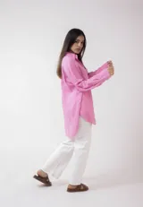 Camisa blanca de lino, de corte holgado, con cuello clásico, cierre frontal con botones, bolsillo en el pecho y mangas largas con puños abotonados.