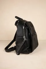 Mochila negra de cuero sintético con diseño minimalista, formato compacto y estructura blanda. Incluye bolsillo delantero con broche y cierre metálico superior con tiradores largos.