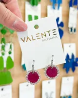 Par de aros colgantes plateados con forma circular y centro fucsia rodeado de strass.