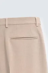 Pantalón de vestir color beige, corte slim fit, confeccionado en tejido con viscosa. Cuenta con bolsillos frontales y traseros de doble vivo con botón. Cierre frontal con cremallera y botón.