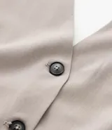 Chaleco color beige con escote halter, corte al cuerpo y cierre frontal con botones. Presenta un bolsillo de ojal en el frente.