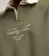 Sweater verde oliva de algodón y poliéster con cuello polo blanco, mangas largas y lettering bordado en el frente.