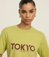 Remera verde claro de algodón con cuello redondo y mangas cortas. Estampado frontal con la palabra "TOKYO" en color borgoña y la frase "Where Zen Meets The Neón" debajo.