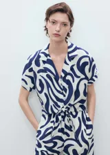 Camisa de viscosa blanca con estampado abstracto en azul, corte crop, cuello camisero, mangas cortas y nudo decorativo en el frente.