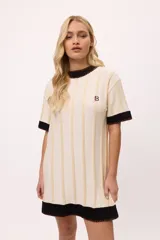 Vestido de tejido de punto color amarillo con rayas verticales en tono más claro. Presenta cuello redondo y puños en color celeste con terminación de pespunte en color naranja. Lleva un bordado de iniciales en el pecho.