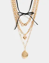 Set de tres collares dorados con diferentes tipos de cadenas y dijes: gargantilla de terciopelo negro con lazo, cadena con dije de corazón y cadena con relicario ovalado con diseño floral.