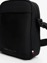 Bandolera Tommy Hilfiger negra con correa ajustable, cierre de cremallera, bolsillo interior abierto, bolsillo exterior con cremallera y logo metálico en el frente.