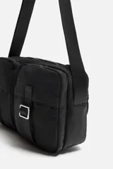 Bandolera negra de tela técnica con correa ajustable. Tiene un compartimento principal con cierre de cremallera, un bolsillo interior con cremallera y dos bolsillos frontales con cierre de hebilla.