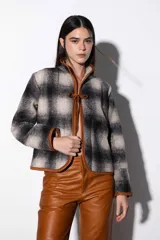 Chaqueta corta de paño a cuadros en tonos beige y negro, con ribete de cuero marrón en todo el contorno y cierre con lazos de cuero. Tiene dos bolsillos laterales.