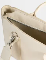 Cartera tipo tote color blanco crudo, con doble asa corta y correa larga regulable y desmontable. Incluye charm colgante con forma de corazón y cierre superior.