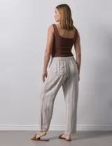 Pantalón de lino a rayas verticales color beige y blanco, con pretina ancha elastizada, lazo de ajuste y bolsillos inclinados.