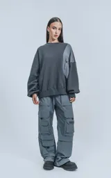 Buzo gris oscuro de cuello redondo, corte oversize y largo crop. Presenta un bolsillo grande de microfibra gris claro en el frente.