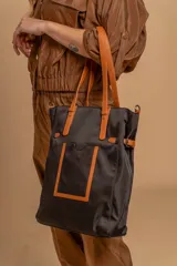 Cartera tipo tote bag color negro, con doble asa de mano y correa bandolera ajustable. Presenta un bolsillo rectangular en el frente.