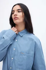 Camisa celeste de denim de algodón, con cuello solapa clásico, bolsillo cuadrado en el pecho, botones personalizados y calce oversize.