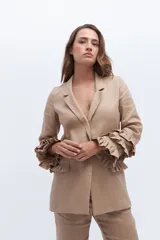 Blazer color beige confeccionado en lino, con cuello solapa, cierre frontal con un botón y mangas largas con volantes en capas.