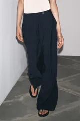 Pantalón de tiro medio color celeste confeccionado en hilatura con mezcla de lyocell. Tiene bolsillos laterales, pinzas delanteras, pierna ancha y cierre frontal con cremallera y botón.