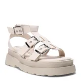 Sandalias bajas color beige con plataforma y tiras anchas con hebillas plateadas, estilo romano.