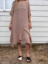 Vestido de tela liviana color marrón topo, con escote redondo y manga corta. Presenta una hilera de botones marrones en el frente y un ruedo asimétrico con capas superpuestas.