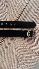 Cinturón negro de cuero con hebilla circular dorada.