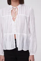 Blusa blanca con rayas verticales, cuello con lazo, mangas largas y corte holgado.
