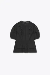 Blusa negra de algodón con cuello redondo y manga corta abullonada. Presenta bordados a tono y cierre en la espalda con abertura y botón.