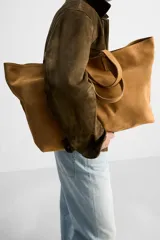 Bolso tipo shopper color marrón claro, fabricado en piel con acabado serraje. Tiene un compartimento principal con cierre imantado y un bolsillo interior con cremallera. Cuenta con dos asas de mano fabricadas en piel.