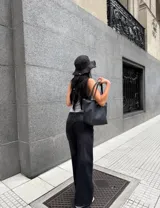 Pantalón de denim rígido negro, tiro alto, de corte ancho (wide leg) y largo. Presenta costuras visibles en el frente que simulan un diseño de paneles.