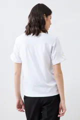 Remera blanca de manga corta con cuello redondo y botón metálico en los puños.