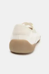 Zapato plano tipo bailarina deportiva, color blanco hueso, con puntera redonda y suela engomada marrón claro. Presenta tiras elásticas cruzadas en el empeine y detalles en gamuza clara.