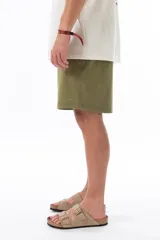 Bermuda verde militar de corte recto, con cintura elástica ajustable con cordón, bolsillos laterales y traseros.