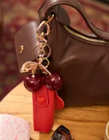 Llavero con dije de cerezas rojas brillantes y mosquetón metálico dorado.